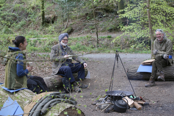 Three people sitting around a campfire drinking tea and laughing