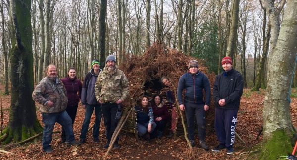 A group of Actif Woods Ceredigion participants standing around a shelter in a woodland