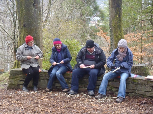 Four people sitting in a woodland doing some wood carving