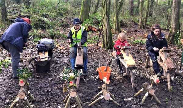 Adults and children doing woodwork in a woodland using shave horses