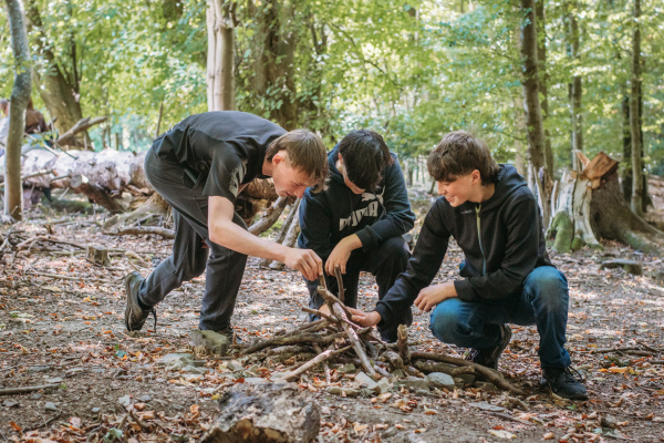 Three young people building a fire in a woodland. They are smiling and enjoying the activity.