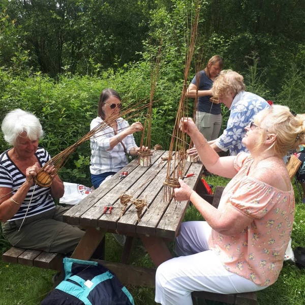 People sitting around a table outdoors making willow baskets