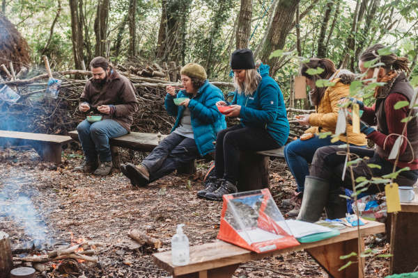 People eating food around a campfire in a woodland