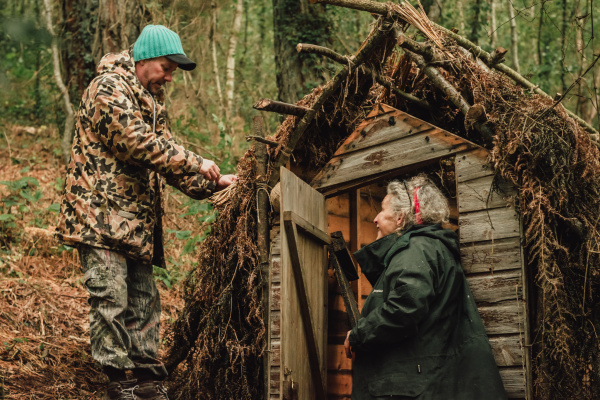 Two people in a woodland building a shelter.